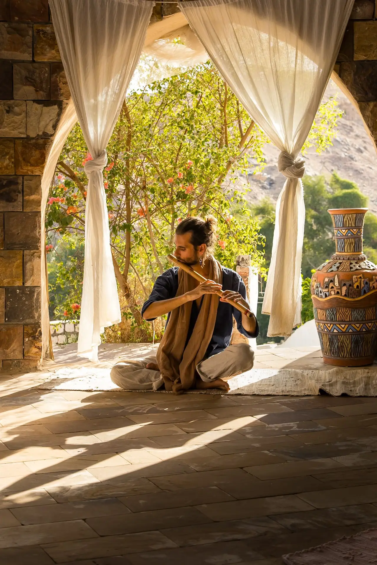 Federico seated on a stone terrace beneath a curtained archway, playing the bansuri