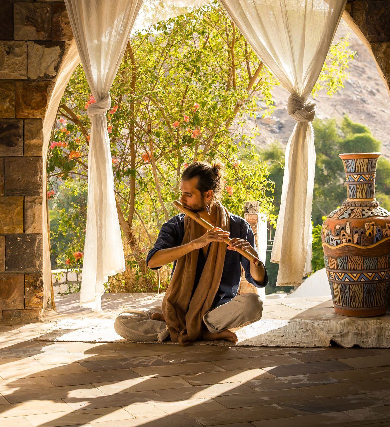 Federico playing the bansuri beneath a stone archway with white curtains