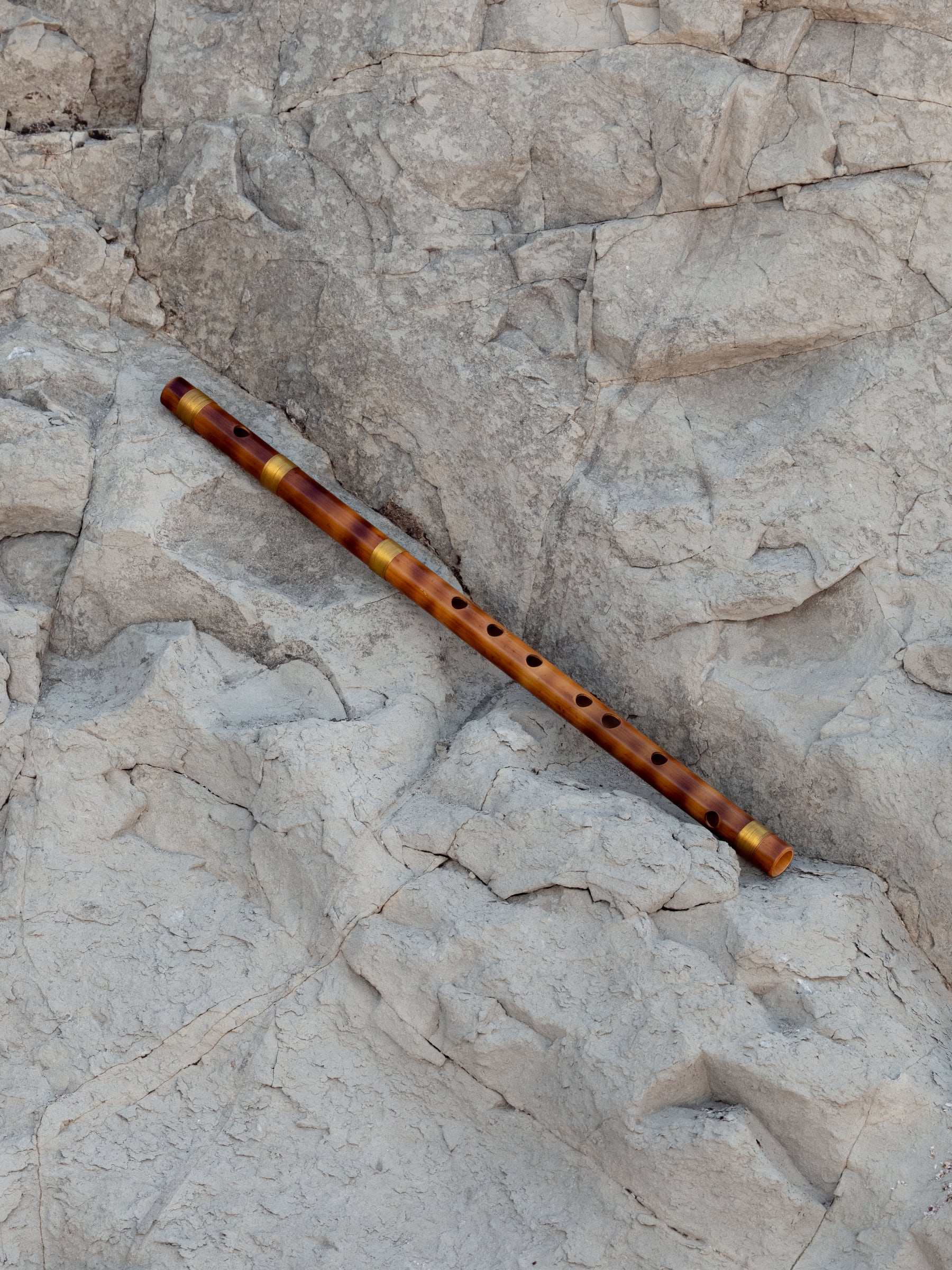 A bamboo bansuri lying diagonally across pale rock