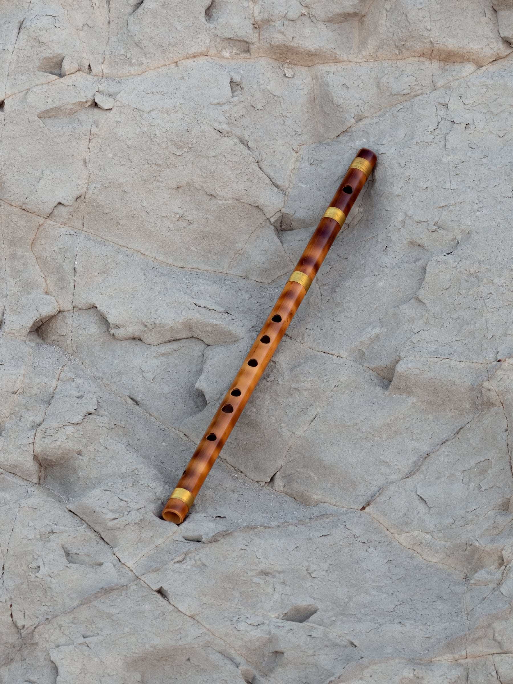 A bamboo bansuri lying across pale rock
