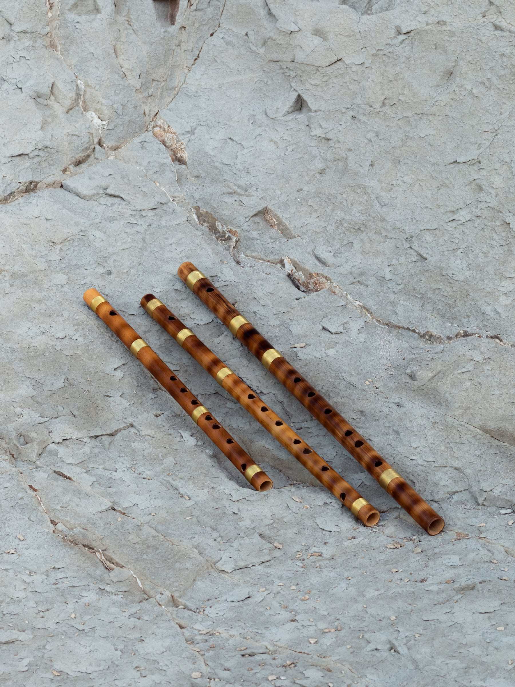 Three bamboo bansuri flutes of different lengths lying side by side on pale rock