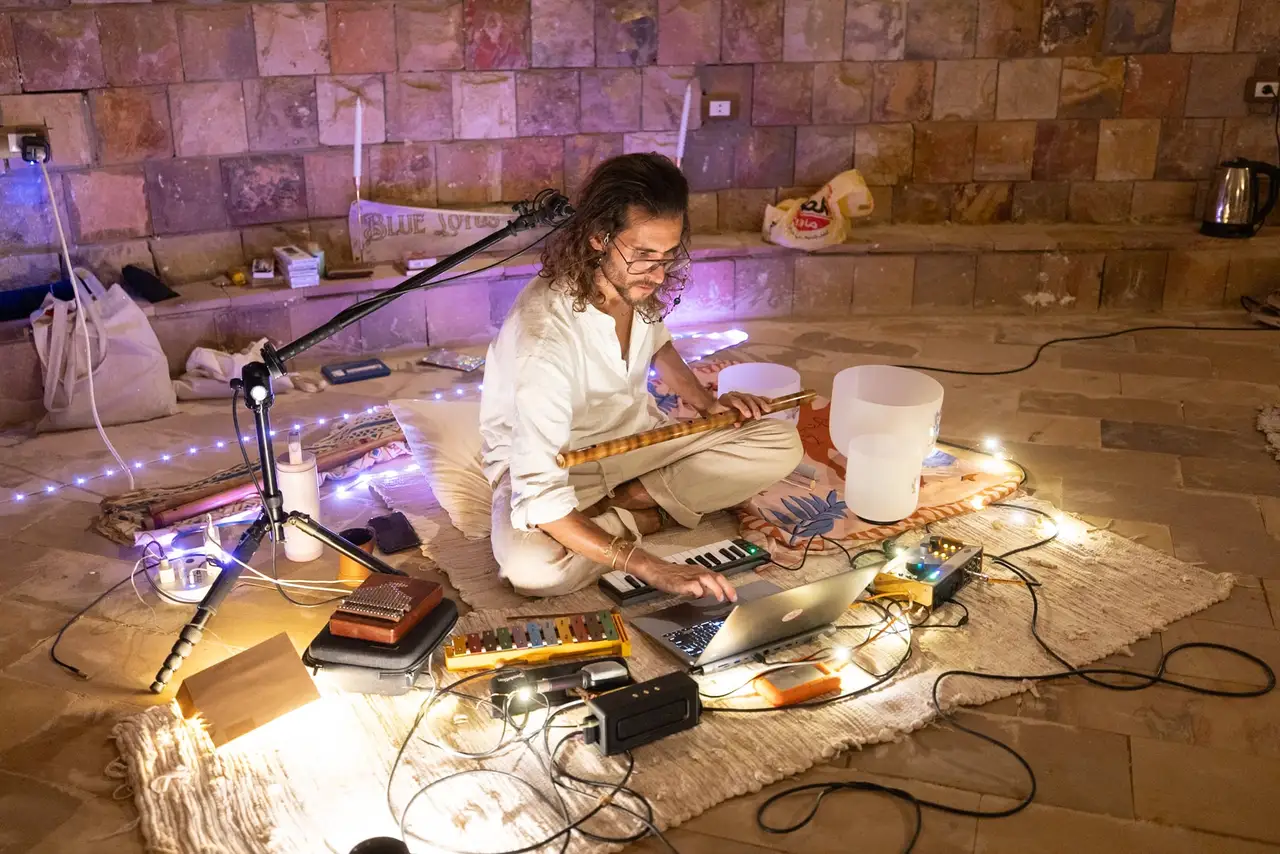 Federico seated among crystal singing bowls, a laptop and small lights, holding a bansuri